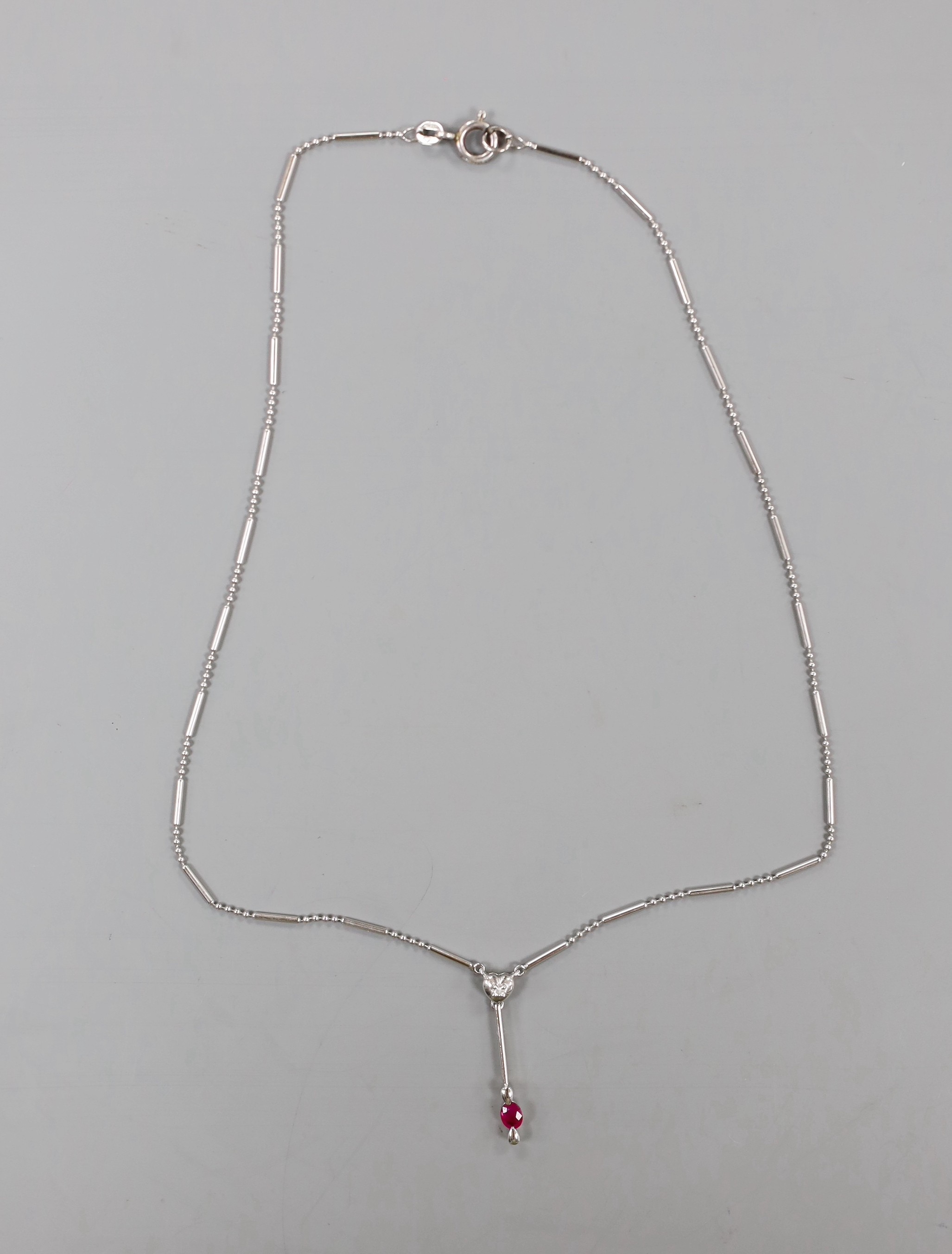 An 18ct white gold (750) pendant with ruby drop on bar and long link chain with silver clasp, chain 38cm, gross 4.8 grams.